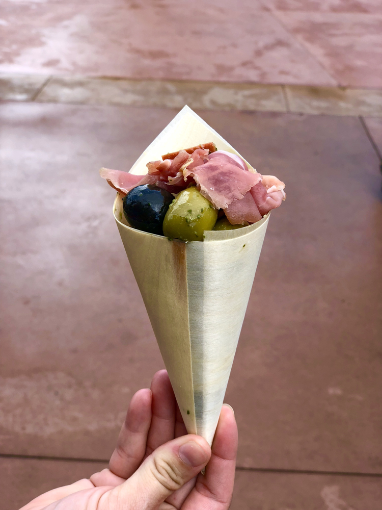 Red meat with green and black olives in a brown cone.