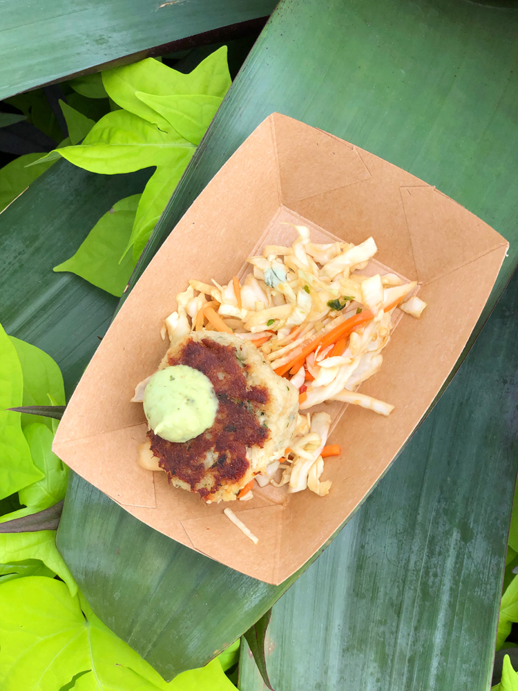 Brown crab cake with green sauce on a big green leaf on a brown dish.