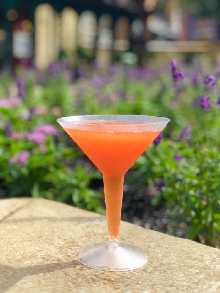 Orange cocktail on a brown ledge in front of purple flowers