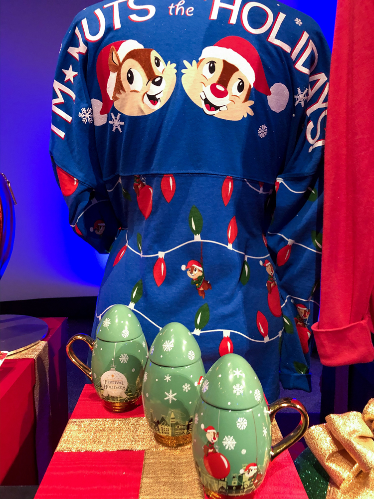 Blue long sleeved top with two chipmunks with Santa hats on and a green mug on a table