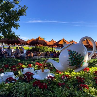 White large teapot pouring into little white teacups in a garden