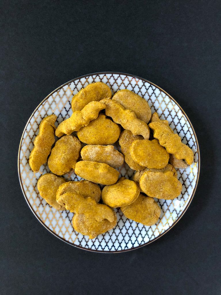 Peanut Butter Pumpkin Dog Treats on a white and gold plate on a black background