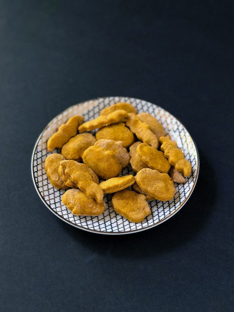 Peanut Butter Pumpkin Dog Treats on a white and gold plate on a black background